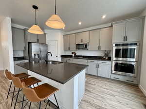 Kitchen featuring appliances with stainless steel finishes, light wood-style floors, hanging light fixtures, gray cabinets, and a kitchen breakfast bar