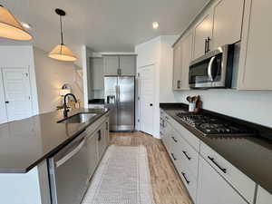 Kitchen with light wood-style floors, appliances with stainless steel finishes, gray cabinetry, pendant lighting, and dark stone countertops
