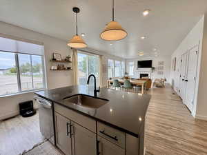 Kitchen featuring a kitchen island with sink, open floor plan, light wood-style flooring, decorative light fixtures, and a textured ceiling