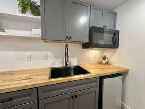 Bar featuring gray cabinetry, butcher block countertops, white fridge, black microwave, and open shelves