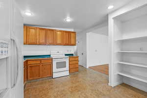 Kitchen featuring white appliances, brown cabinetry, and recessed lighting