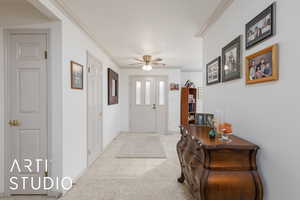 Entrance foyer featuring ornamental molding, a ceiling fan, light carpet, and light tile patterned flooring