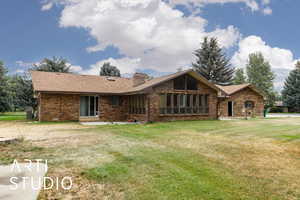 Back of property featuring brick siding, a lawn, a chimney, and a shingled roof