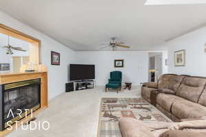 Carpeted living room with ceiling fan, a fireplace, and ornamental molding