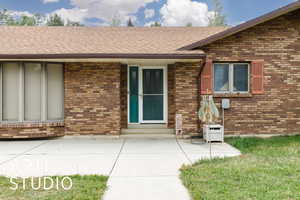 Doorway to property with brick siding, a shingled roof, and a yard