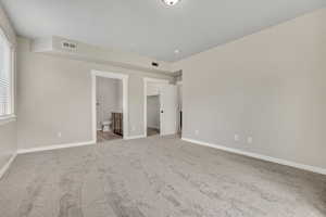 Unfurnished bedroom featuring a walk in closet, light colored carpet, and ensuite bath