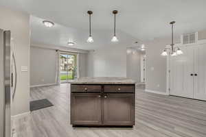 Kitchen with dark brown cabinets, hanging light fixtures, stainless steel fridge, a center island, and light wood finished floors