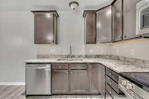 Kitchen with appliances with stainless steel finishes, light stone countertops, dark brown cabinets, and light wood-style floors