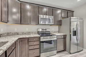 Kitchen featuring appliances with stainless steel finishes, light stone counters, dark brown cabinetry, and light wood finished floors
