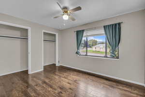 Unfurnished bedroom featuring two closets, dark wood-type flooring, and a ceiling fan