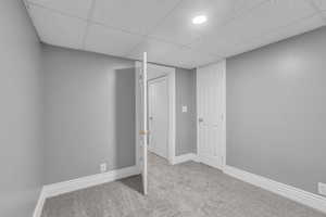 Finished below grade area featuring light colored carpet and a drop ceiling