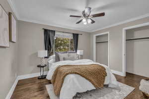 Bedroom featuring two closets, crown molding, dark wood finished floors, and ceiling fan