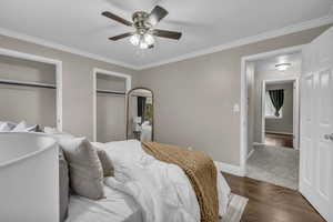 Bedroom featuring ornamental molding, dark wood finished floors, two closets, and ceiling fan