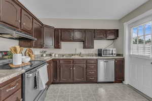 Kitchen featuring dark brown cabinetry, stainless steel appliances, under cabinet range hood, and light countertops