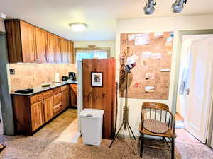 Kitchen with light tile patterned floors, brown cabinets, backsplash, light carpet, and rail lighting