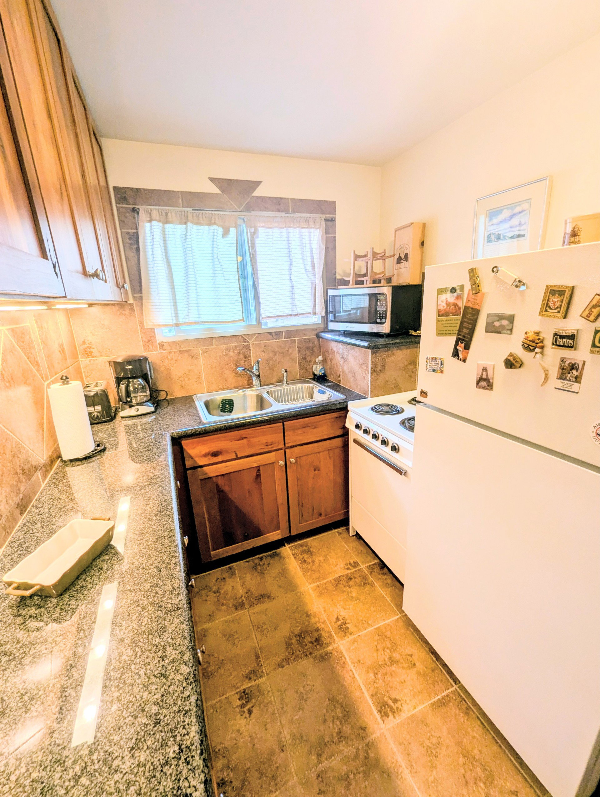 Kitchen featuring white appliances, tasteful backsplash, dark stone countertops, brown cabinets, and light tile patterned flooring