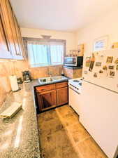 Kitchen featuring white appliances, tasteful backsplash, dark stone countertops, brown cabinets, and light tile patterned flooring