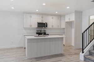Kitchen with recessed lighting, appliances with stainless steel finishes, an island with sink, light wood-style floors, and light stone counters