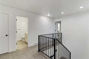 Hall with an upstairs landing, light colored carpet, recessed lighting, and a textured ceiling