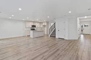 Kitchen featuring open floor plan, a center island with sink, light countertops, recessed lighting, and light wood-type flooring