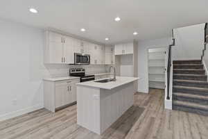 Kitchen with appliances with stainless steel finishes, recessed lighting, a center island with sink, light wood-style flooring, and light stone countertops