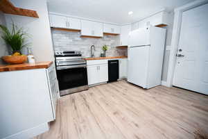 Kitchen featuring butcher block countertops, tasteful backsplash, freestanding refrigerator, white cabinets, and recessed lighting