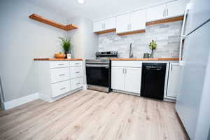 Kitchen featuring freestanding refrigerator, white cabinetry, stainless steel electric range oven, decorative backsplash, and dishwasher