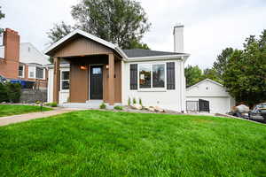 View of front of property featuring a chimney, an outdoor structure, a garage, a shingled roof, and brick siding