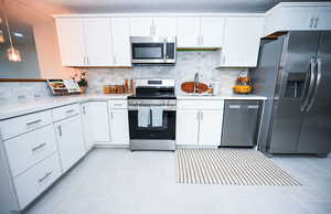 Kitchen featuring appliances with stainless steel finishes, white cabinetry, and tasteful backsplash