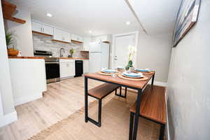 Kitchen with white cabinetry, decorative backsplash, light wood finished floors, electric range, and freestanding refrigerator