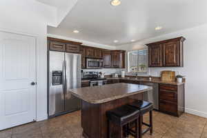 Kitchen featuring dark brown cabinets, stainless steel appliances, a kitchen island, a breakfast bar, and dark countertops