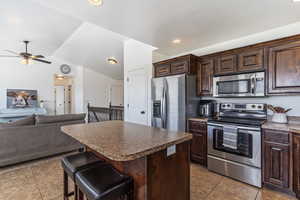 Kitchen with appliances with stainless steel finishes, dark brown cabinets, open floor plan, a center island, and a breakfast bar
