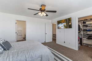 Carpeted bedroom featuring a spacious closet, ceiling fan, and ensuite bathroom