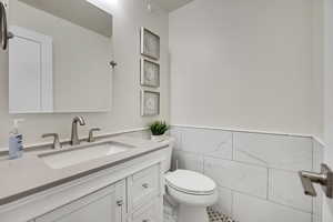 Half bathroom with tile walls, vanity, a wainscoted wall, and tile patterned flooring
