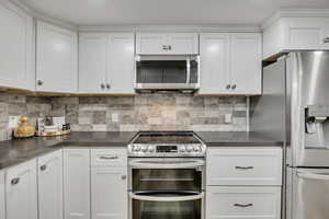 Kitchen with stainless steel appliances, white cabinetry, and decorative backsplash