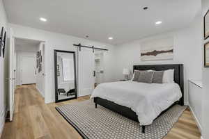 Bedroom with a barn door, recessed lighting, a walk in closet, and light wood-style flooring