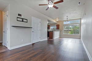 Unfurnished living room with a ceiling fan, dark wood finished floors, and a textured ceiling