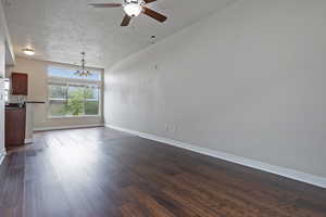 Unfurnished living room featuring a textured ceiling, dark wood-style floors, a ceiling fan, and a chandelier