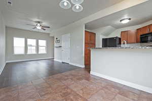 Kitchen with a textured ceiling, black appliances, brown cabinets, open floor plan, and a ceiling fan