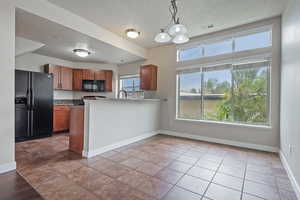 Kitchen featuring brown cabinetry, black appliances, decorative light fixtures, a textured ceiling, and a peninsula