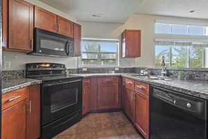 Kitchen featuring black appliances, plenty of natural light, a textured ceiling, dark stone counters, and dark brown cabinets