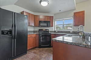 Kitchen featuring black appliances, a textured ceiling, dark stone countertops, and brown cabinetry