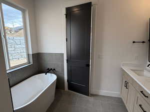 Full bath featuring a freestanding bath, healthy amount of natural light, vanity, light tile patterned floors, and tile walls
