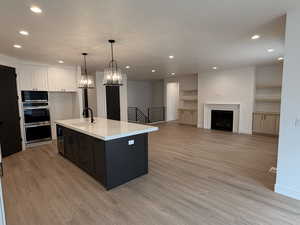 Kitchen featuring decorative light fixtures, a kitchen island with sink, light wood-style floors, open floor plan, and white cabinets