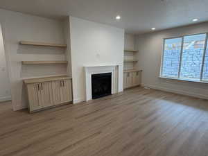 Unfurnished living room featuring a textured ceiling, light wood-style floors, a fireplace with flush hearth, and recessed lighting