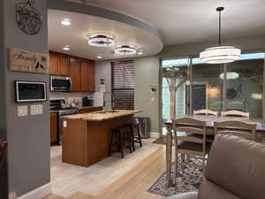 Kitchen featuring light stone countertops, stainless steel appliances, light wood-style flooring, a breakfast bar, and a center island with sink