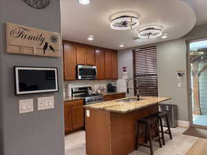 Kitchen with decorative backsplash, light stone counters, brown cabinetry, a breakfast bar area, and stainless steel appliances