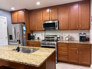 Kitchen featuring light stone counters, brown cabinetry, appliances with stainless steel finishes, tasteful backsplash, and recessed lighting