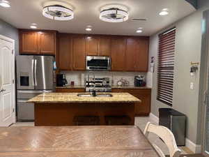 Kitchen with light stone counters, backsplash, stainless steel appliances, recessed lighting, and a kitchen island with sink