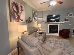 Living room featuring wood finished floors, a glass covered fireplace, and ceiling fan